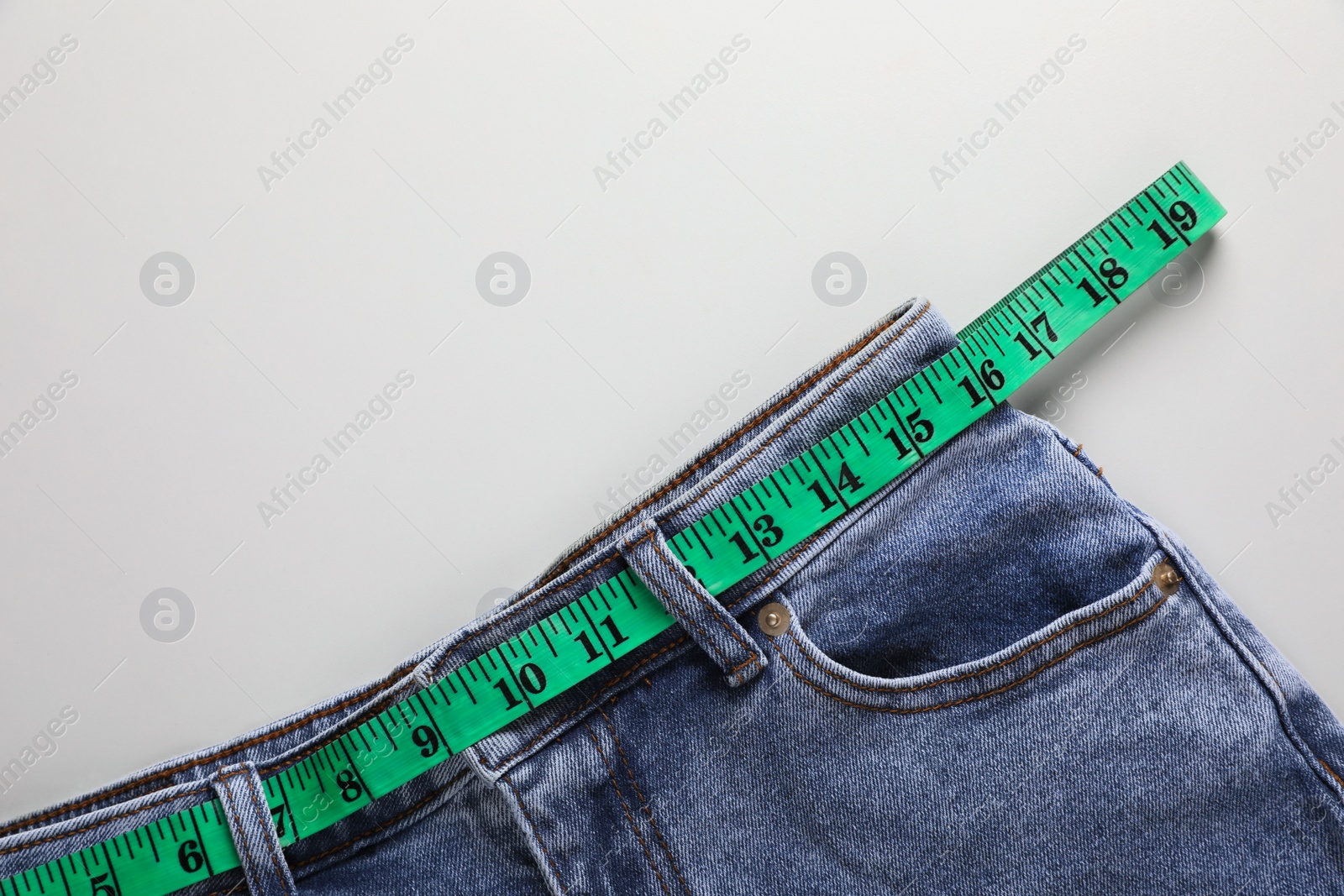 Photo of Jeans with measuring tape on light grey background, top view and space for text. Weight loss concept