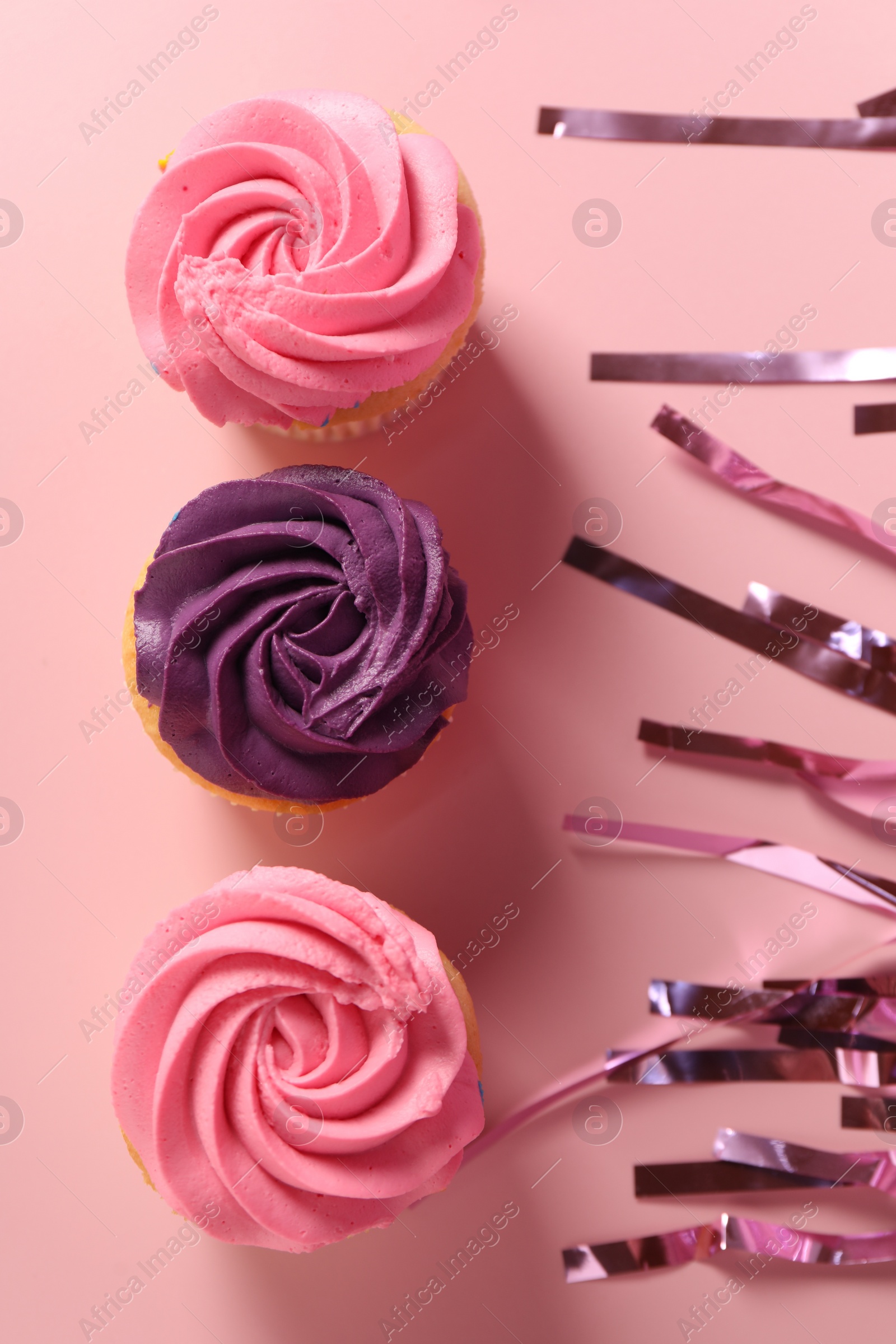 Photo of Delicious cupcakes with bright cream and confetti on pink background, flat lay