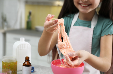 Photo of Little girl kneading DIY slime toy at table in kitchen, closeup
