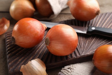 Photo of Many ripe onions and knife on wooden table, closeup