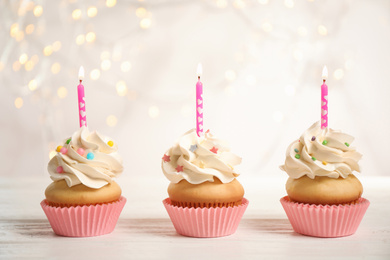 Photo of Birthday cupcakes with candles on white wooden table against blurred lights