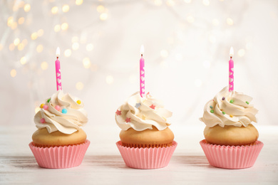 Birthday cupcakes with candles on white wooden table against blurred lights