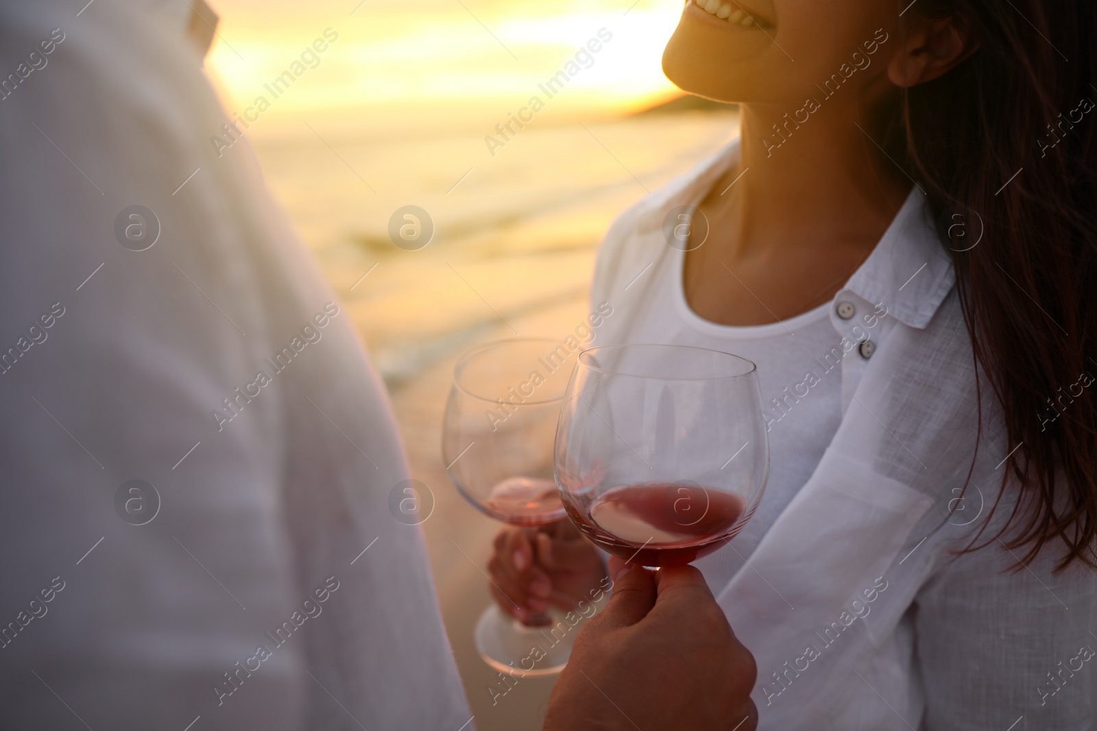 Photo of Couple with glasses of wine on beach at sunset, closeup