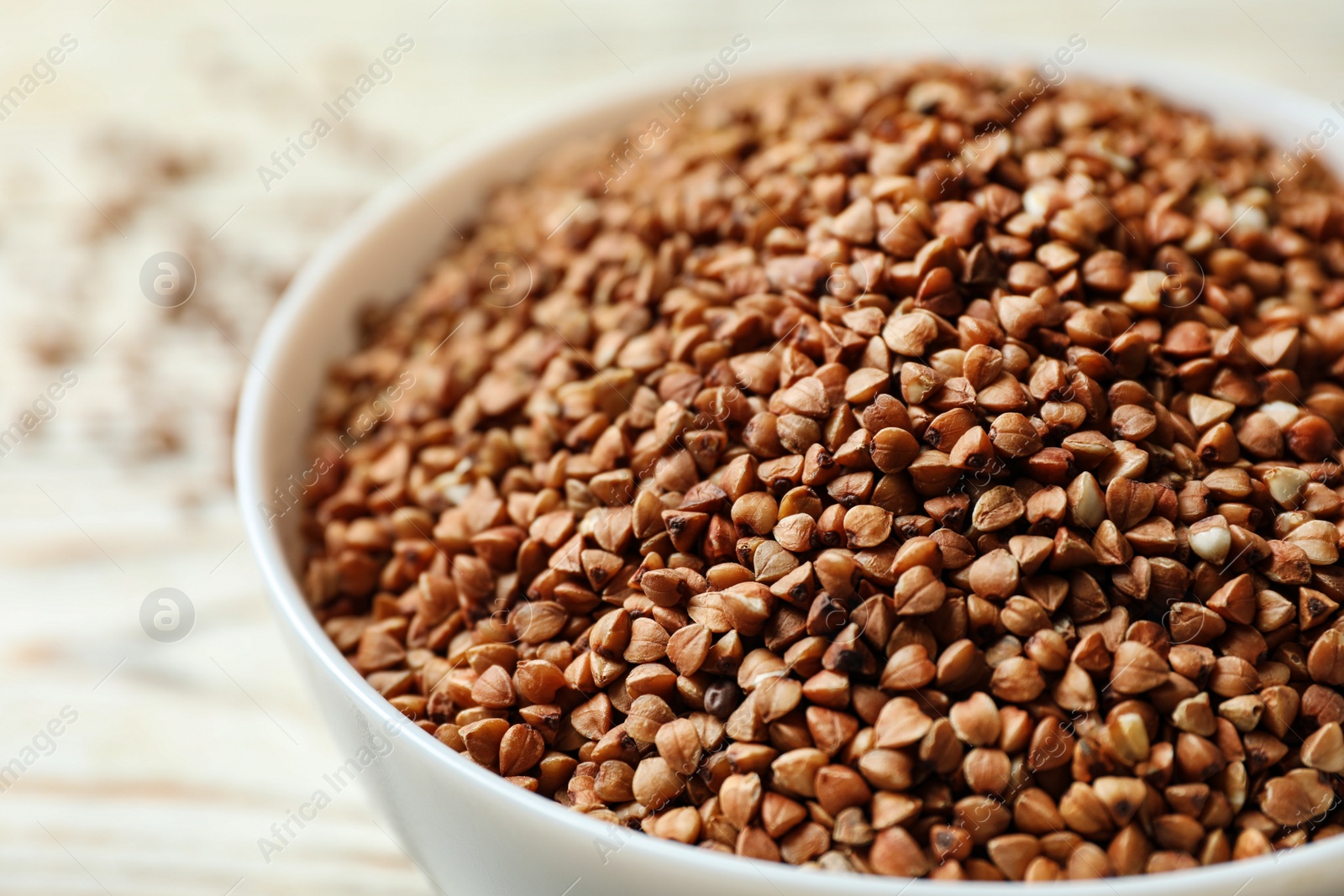 Photo of Bowl of uncooked buckwheat on table, closeup