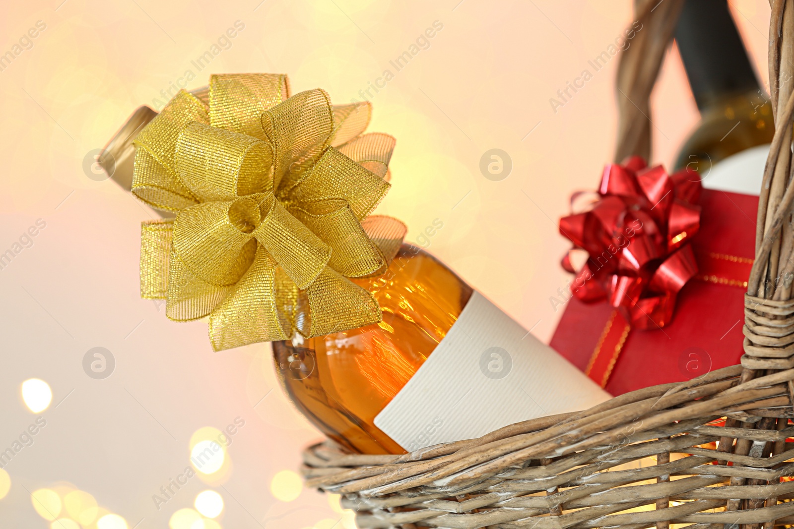 Photo of Wicker basket with bottles of wine and gift box against blurred background, closeup