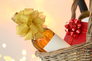 Photo of Wicker basket with bottles of wine and gift box against blurred background, closeup