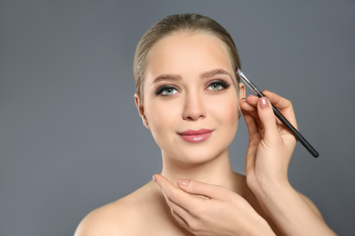 Photo of Artist applying makeup onto woman's face on light grey background