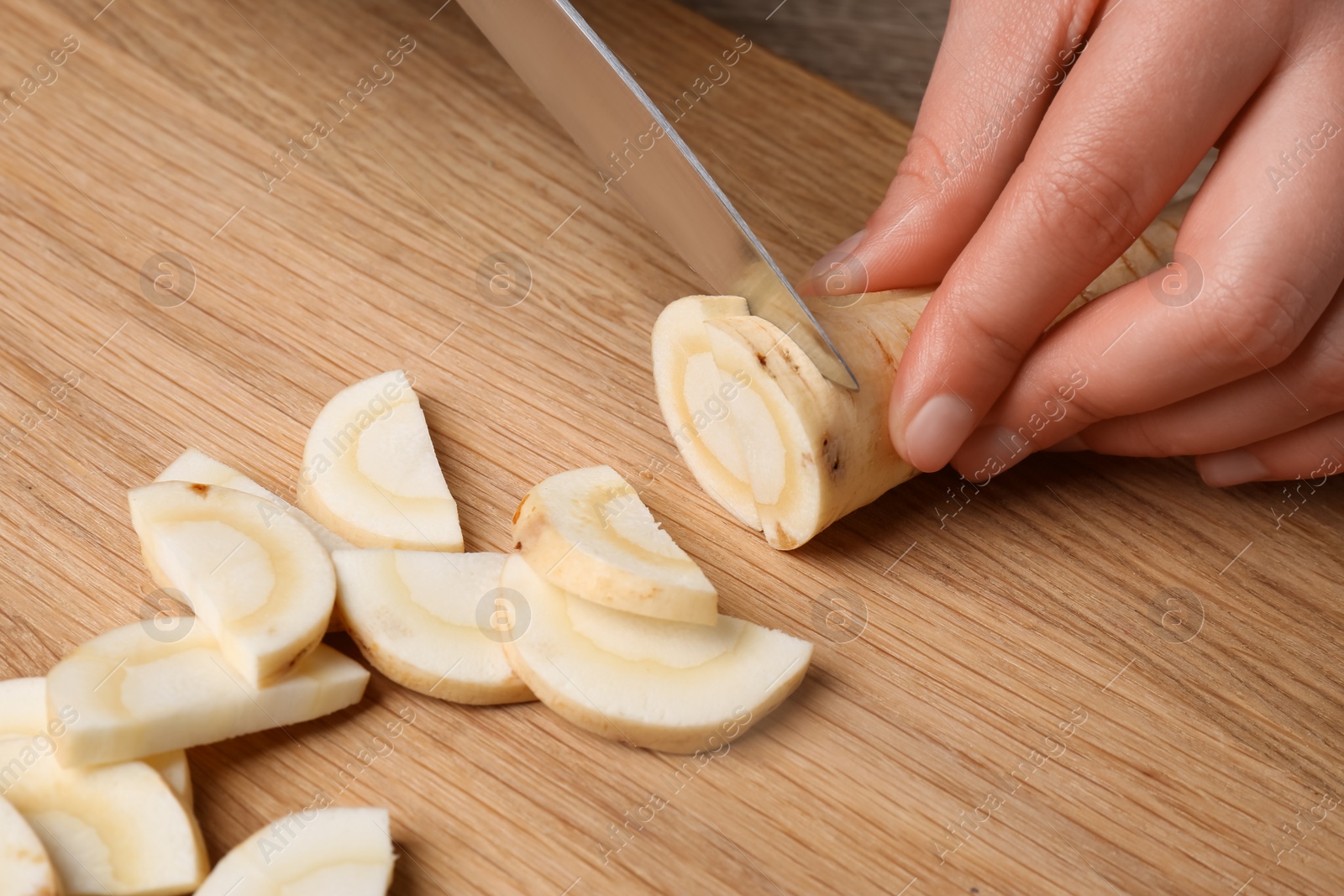 Photo of Woman cutting delicious fresh ripe parsnip at wooden board, closeup