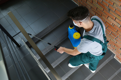 Photo of Pest control worker spraying pesticide on stairs indoors, above view