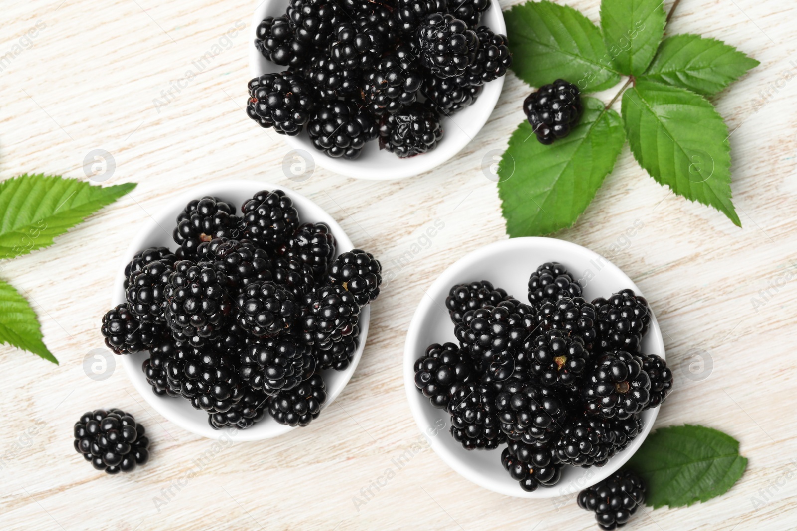 Photo of Ripe blackberries and green leaves on white wooden table, flat lay