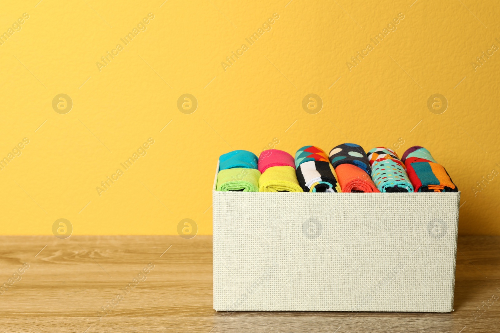 Photo of Box with colorful socks on wooden table against color background