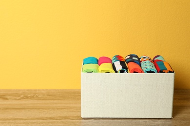 Box with colorful socks on wooden table against color background