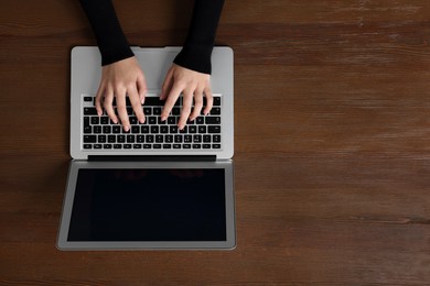 Photo of Woman working with laptop at wooden table, top view. Space for text