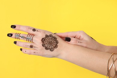 Woman with henna tattoos on hands against yellow background, closeup. Traditional mehndi ornament