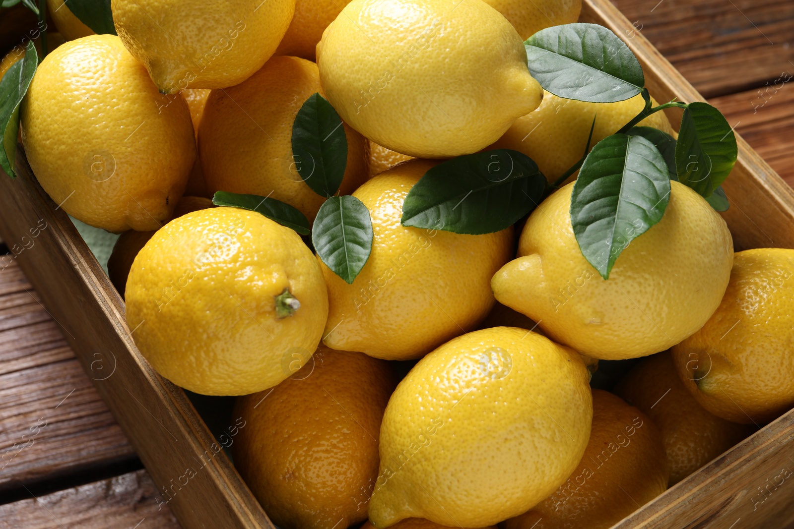 Photo of Fresh lemons in crate on wooden table, closeup