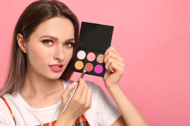 Beauty blogger with brush and eyeshadow palette on pink background