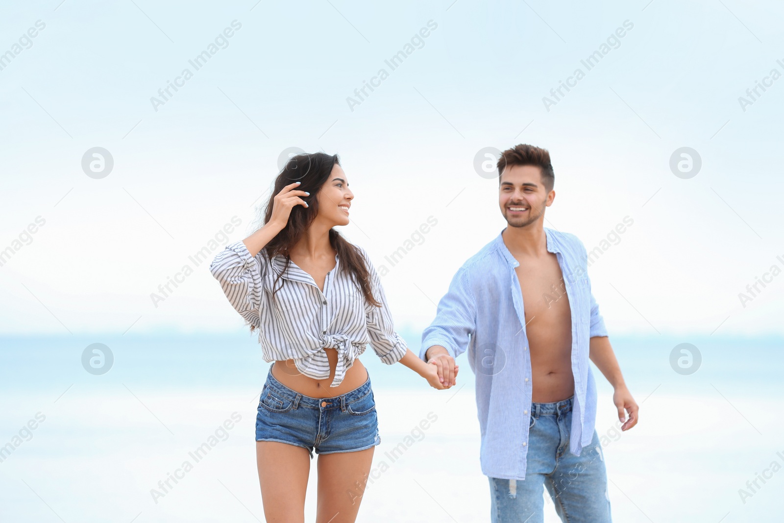 Photo of Happy young couple walking together on beach near sea