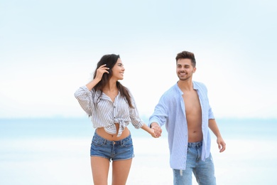 Happy young couple walking together on beach near sea