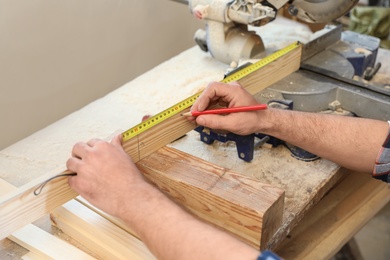 Photo of Working man measuring timber strip in carpentry shop, closeup