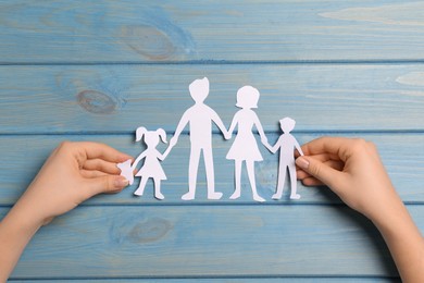 Woman with family paper cutout at light blue wooden table, top view