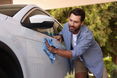 Photo of Bearded man cleaning car door with rag outdoors