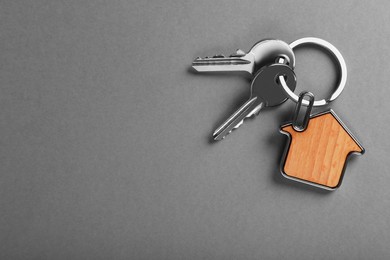 Photo of Keys with trinket in shape of house on grey background, top view and space for text. Real estate agent services