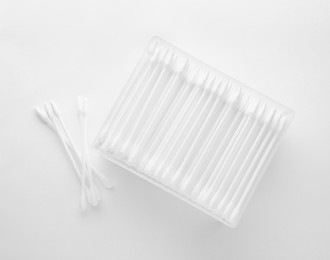 Photo of Cotton buds in plastic container isolated on white, top view