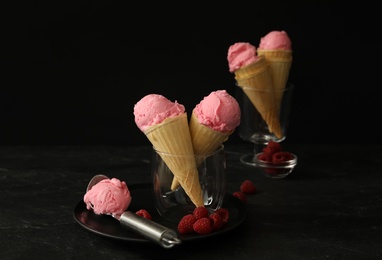 Photo of Delicious pink ice cream in wafer cones and raspberries on black table