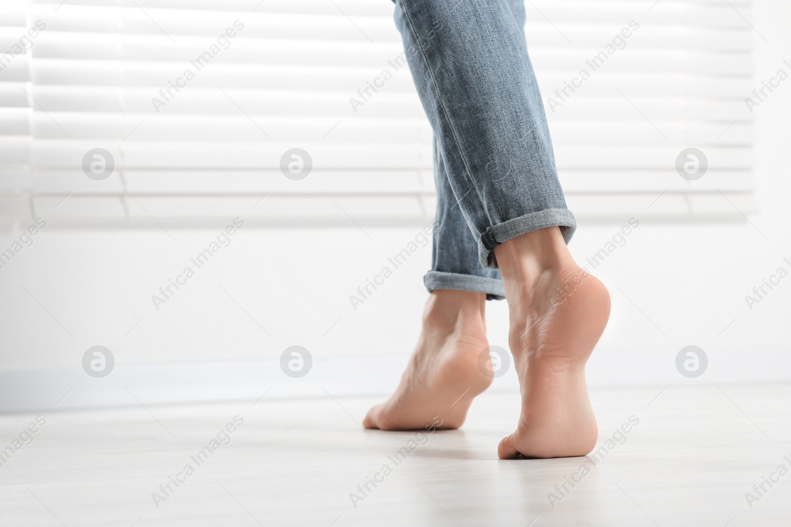 Photo of Barefoot woman walking on white parquet at home, closeup. Heated floor