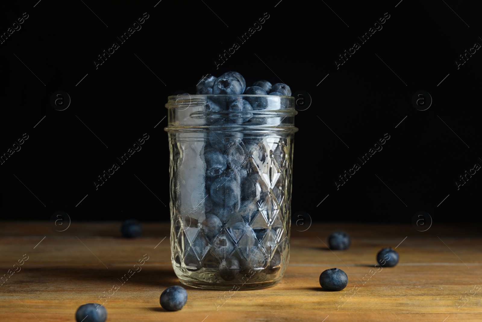 Photo of Tasty ripe blueberries in glass jar on wooden table