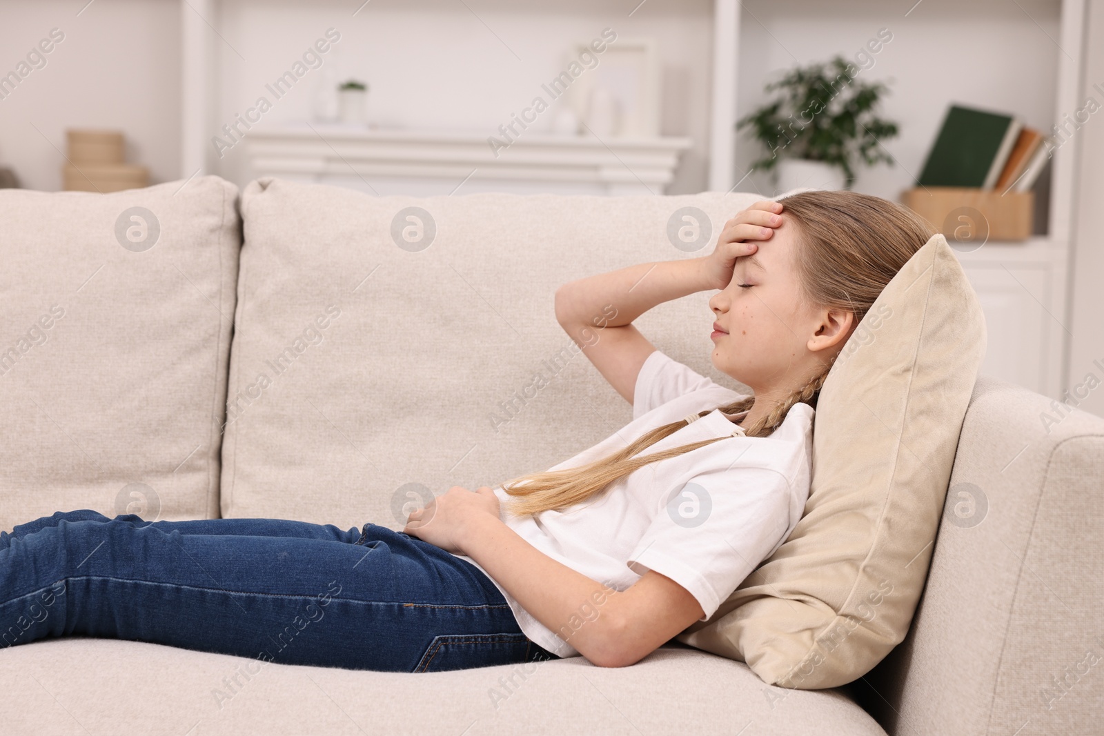 Photo of Little girl suffering from headache on sofa indoors