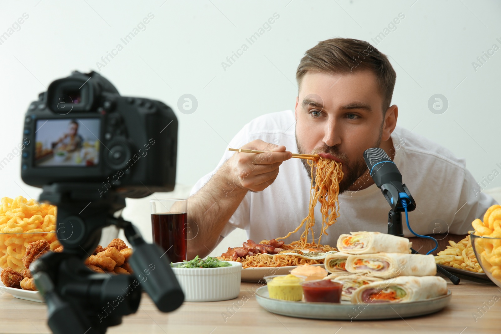 Photo of Food blogger recording eating show on camera against light background. Mukbang vlog