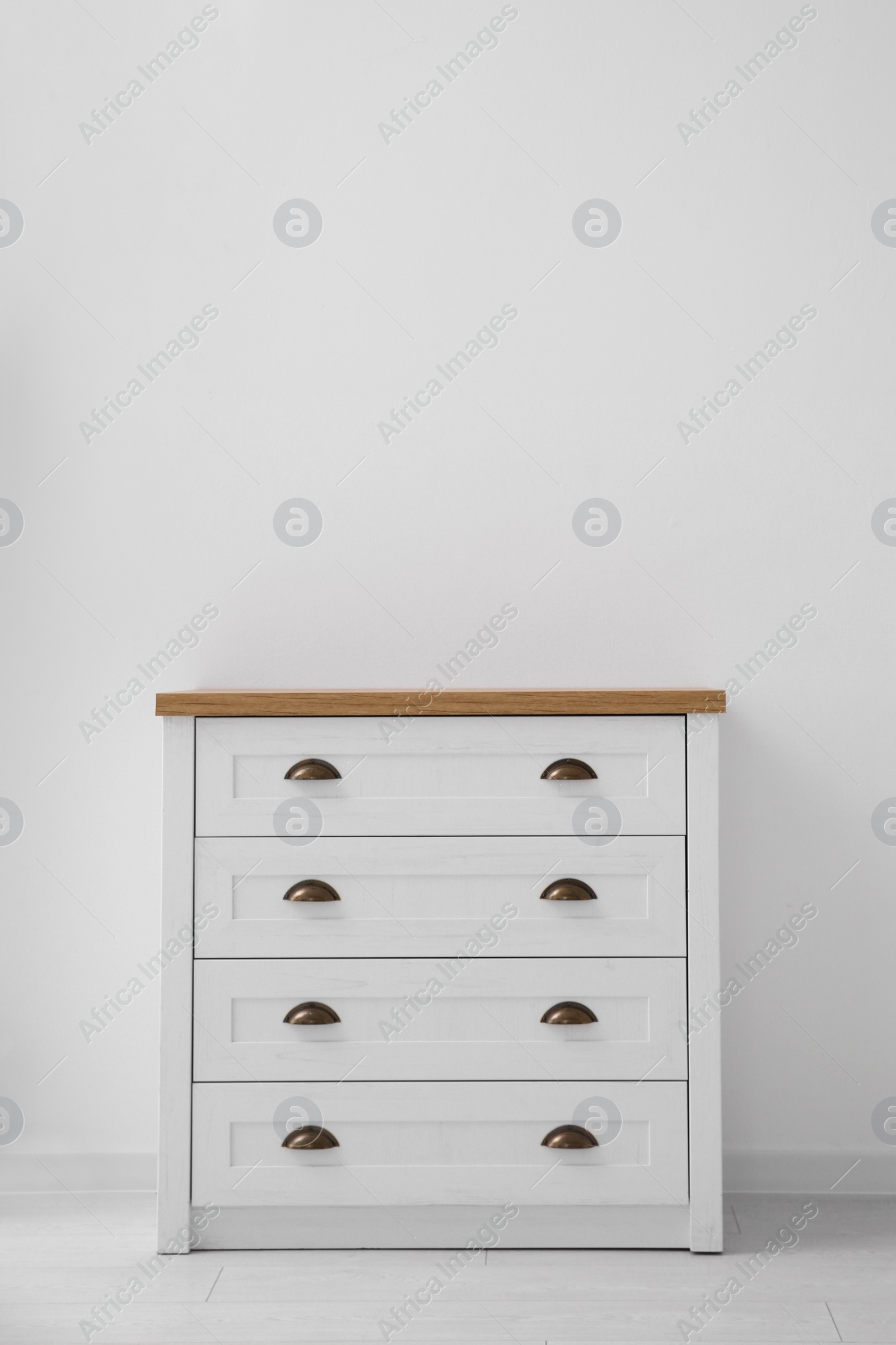 Photo of Modern white chest of drawers near light wall in room, space for text. Interior design