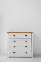 Modern white chest of drawers near light wall in room, space for text. Interior design