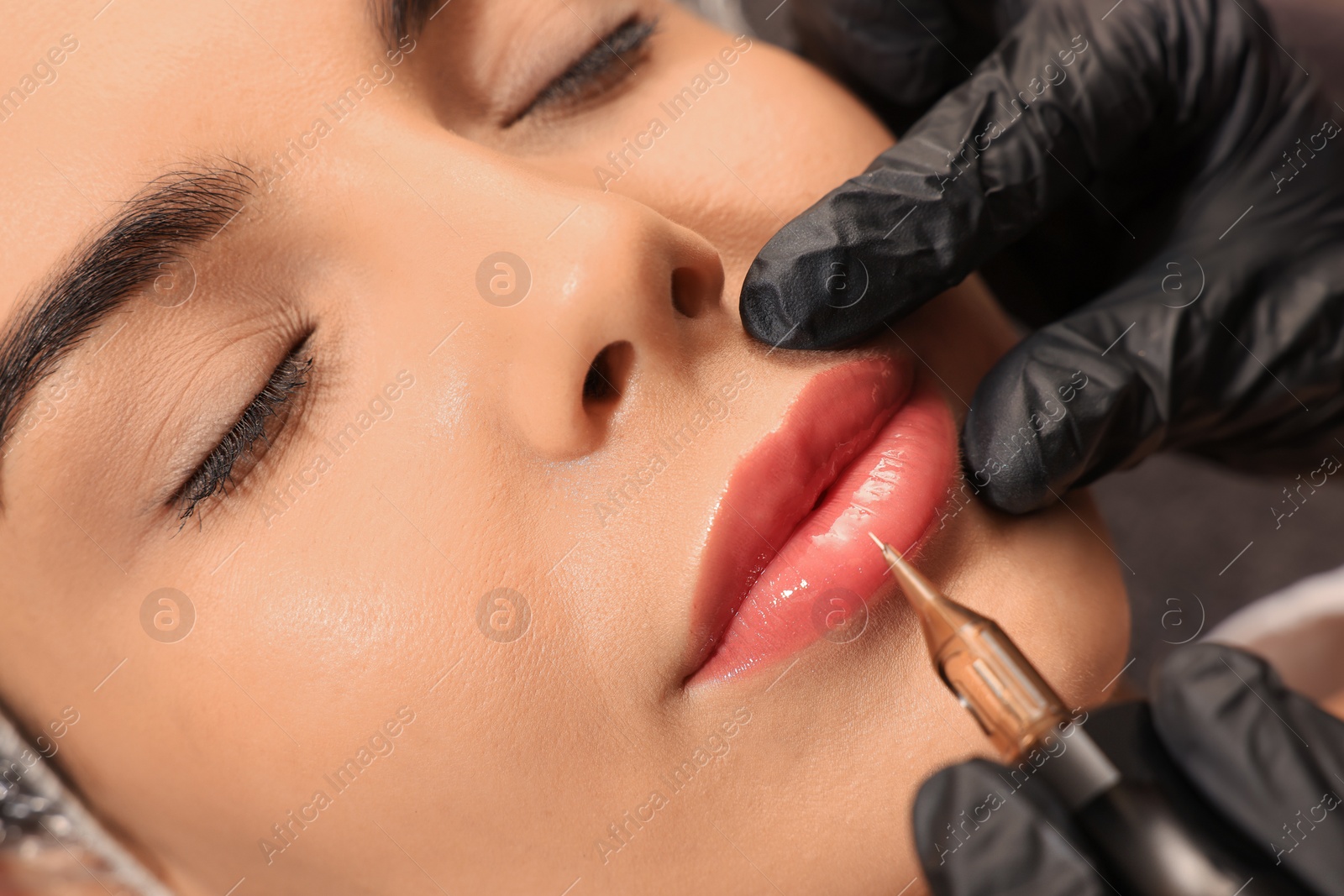 Photo of Young woman undergoing procedure of permanent lip makeup in tattoo salon, closeup