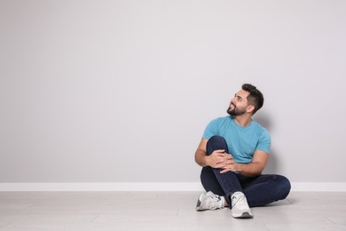 Photo of Young man sitting on floor near light grey wall indoors. Space for text