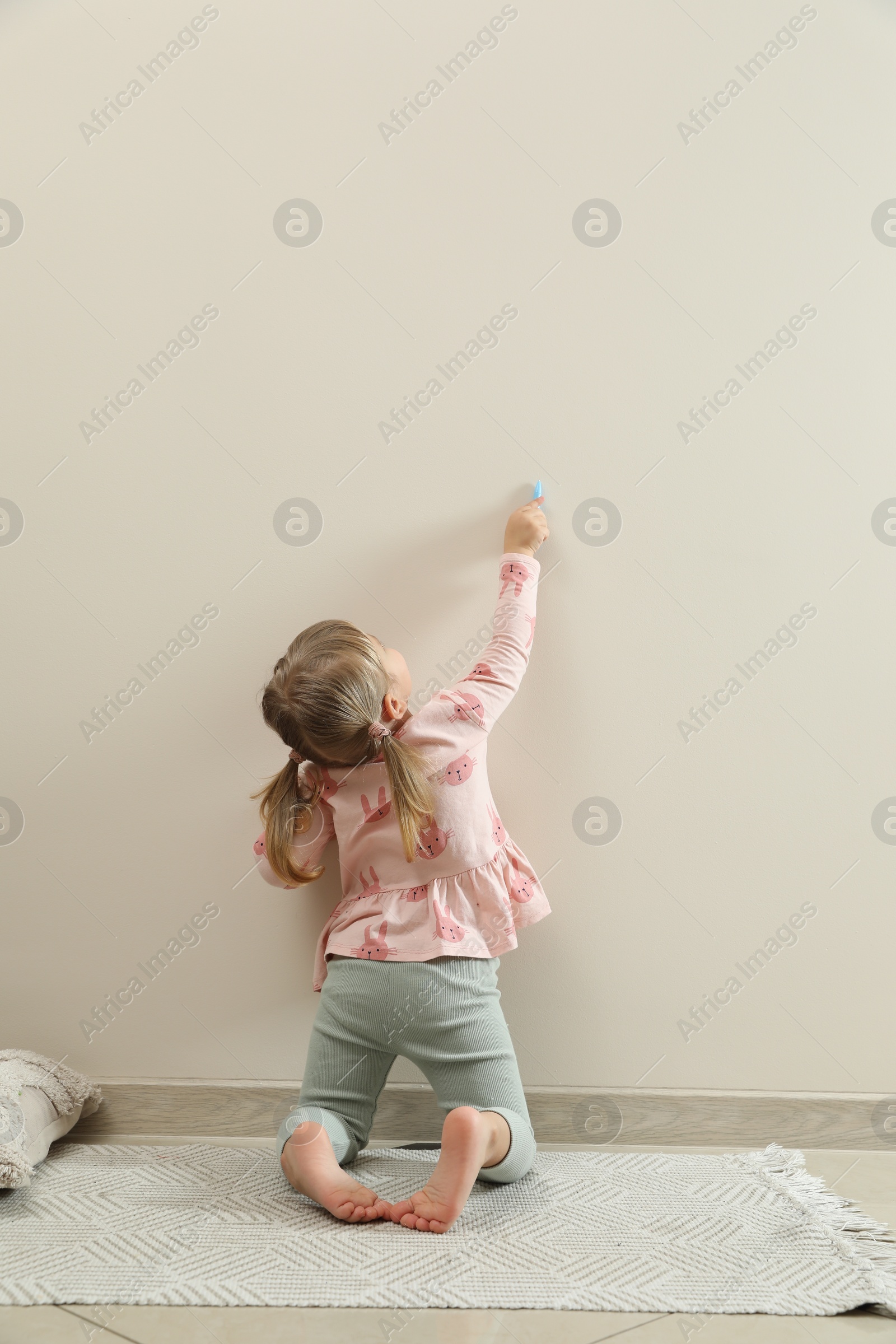 Photo of Little girl drawing on beige wall indoors, back view. Child`s art