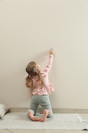 Little girl drawing on beige wall indoors, back view. Child`s art