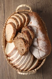 Different types of bread in wicker basket on wooden table, top view