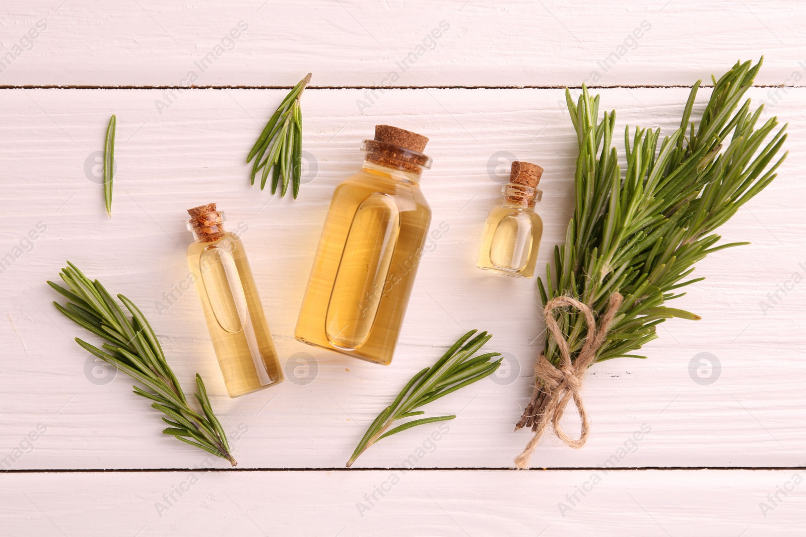 Photo of Essential oil in bottles and rosemary on white wooden table, flat lay