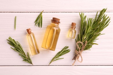 Photo of Essential oil in bottles and rosemary on white wooden table, flat lay