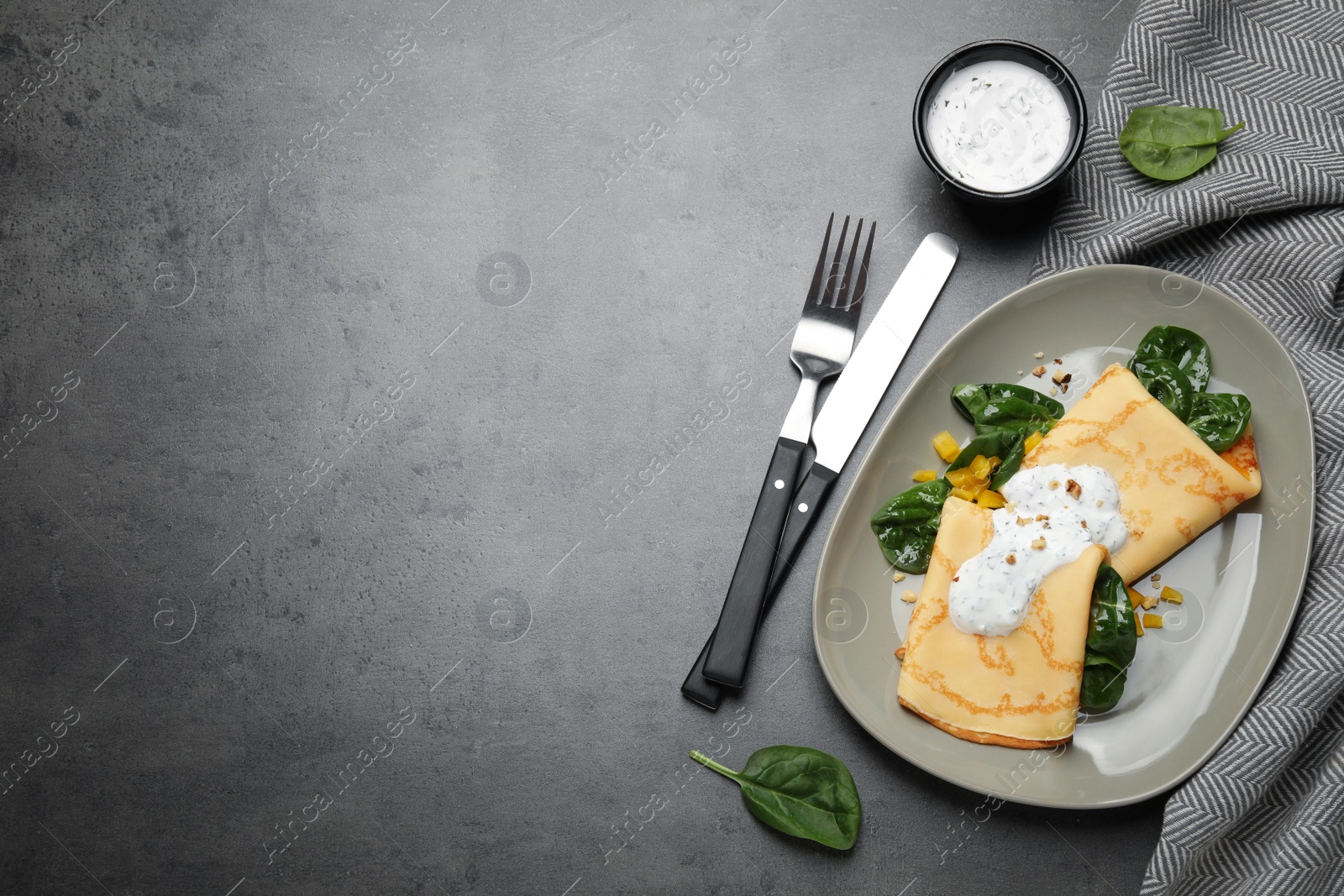 Photo of Delicious thin pancakes with spinach and sour cream on grey table, flat lay. Space for text