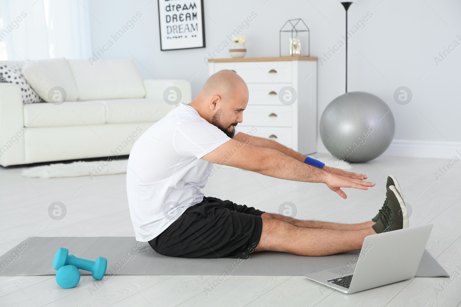 Photo of Overweight man doing exercise while watching tutorial on laptop at home