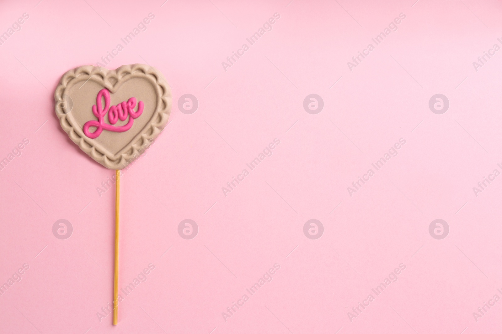 Photo of Chocolate heart shaped lollipop with word Love on light pink background, top view. Space for text
