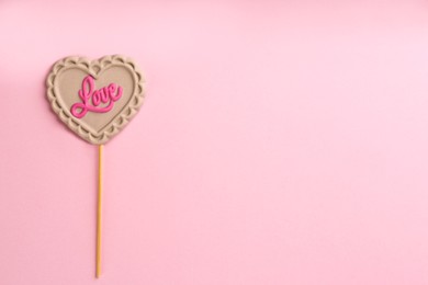 Photo of Chocolate heart shaped lollipop with word Love on light pink background, top view. Space for text