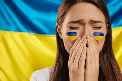 Photo of Sad young woman with clasped hands near Ukrainian flag. Space for text