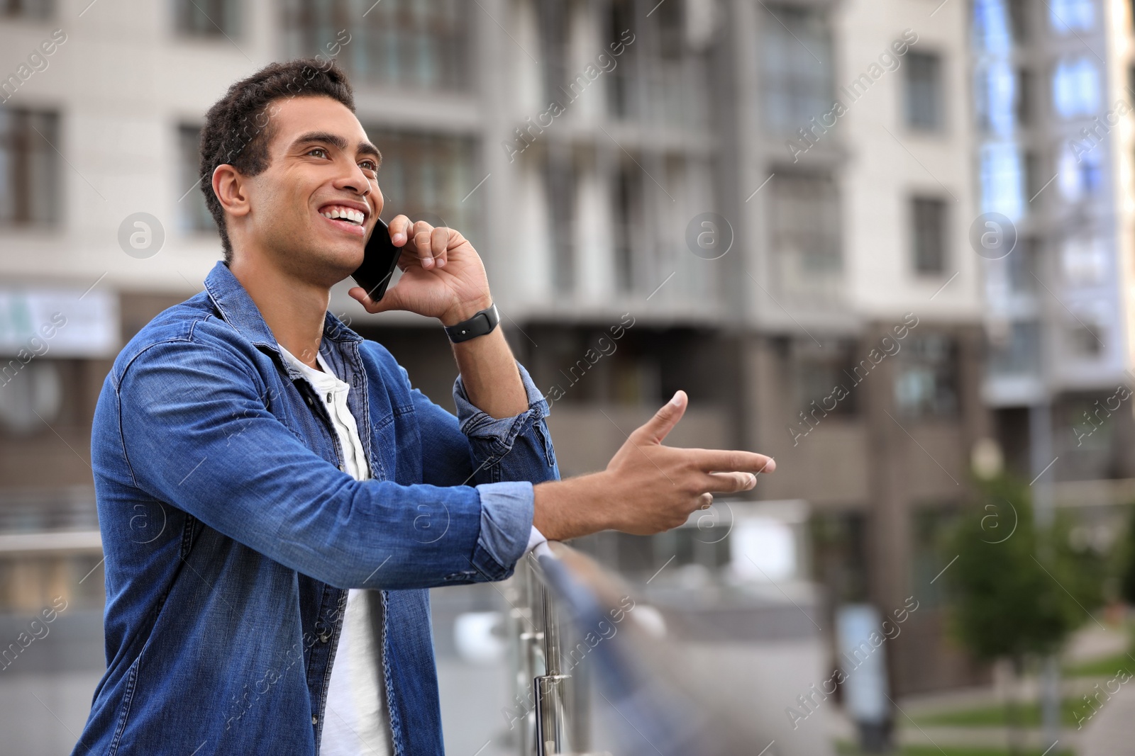 Photo of Handsome young African-American man talking on mobile phone outdoors. Space for text