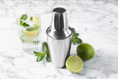 Photo of Metal cocktail shaker, delicious mojito, limes and mint on white marble table