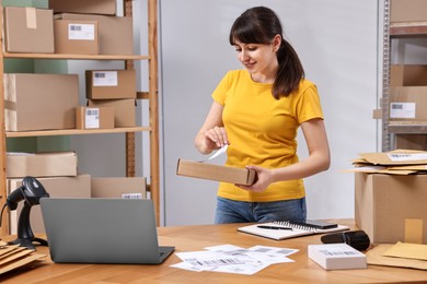 Parcel packing. Post office worker sticking barcode on box at wooden table indoors