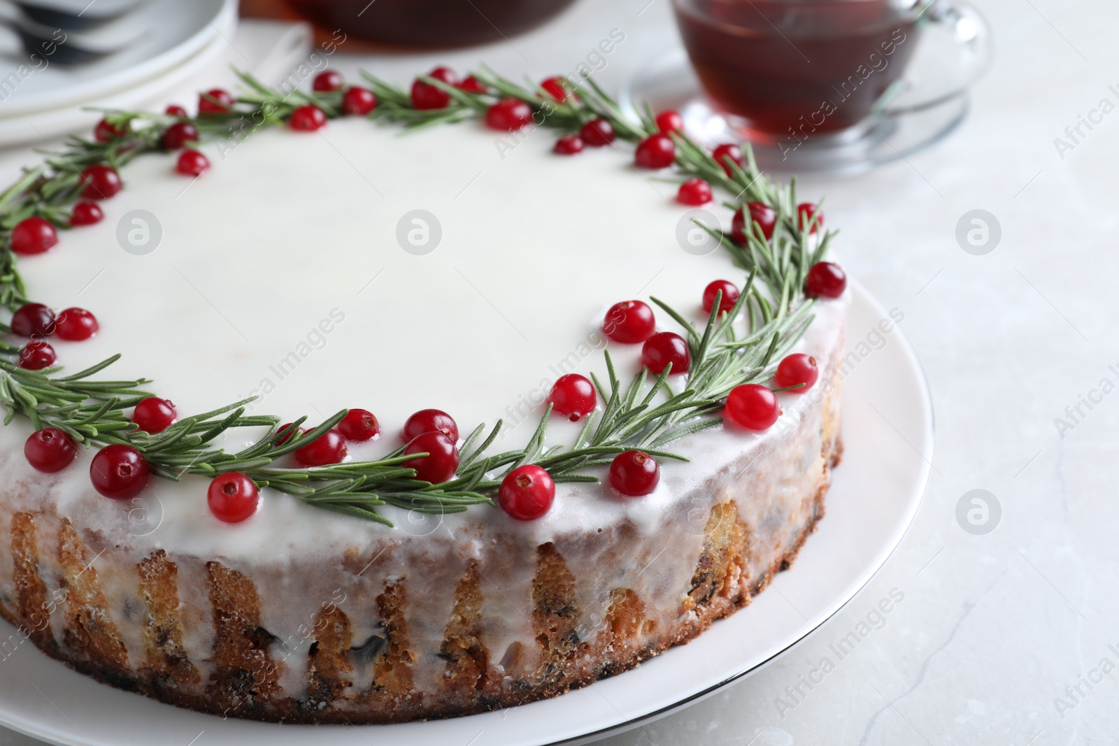 Photo of Traditional Christmas cake decorated with rosemary and cranberries on light table, closeup